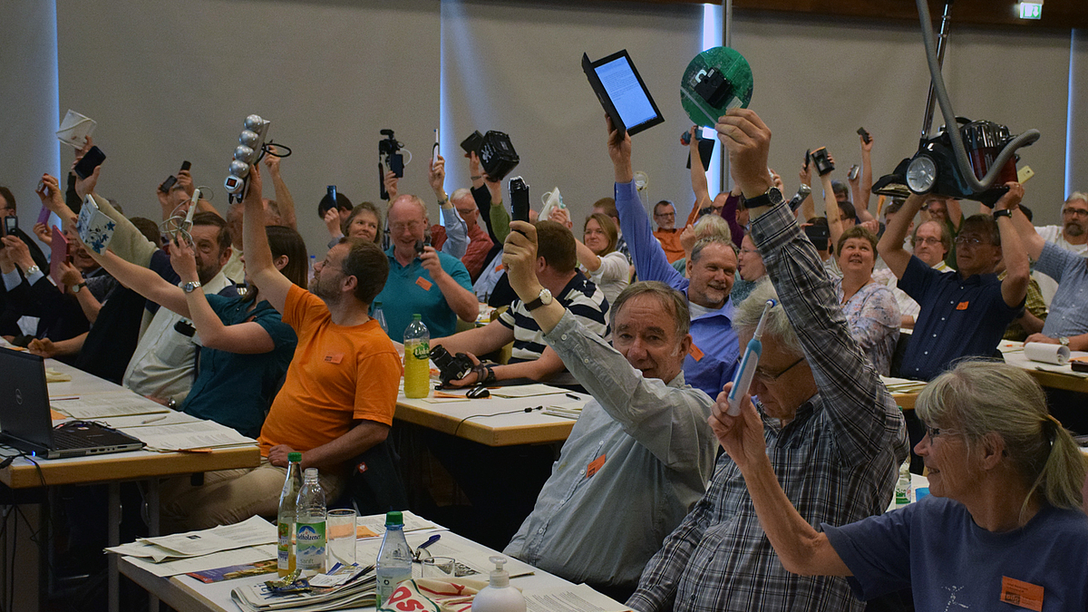 Das Foto zeigt eine Abstimmung in einer Versammlung mit Haushaltsgeräten gegen den konstruierten Schrott